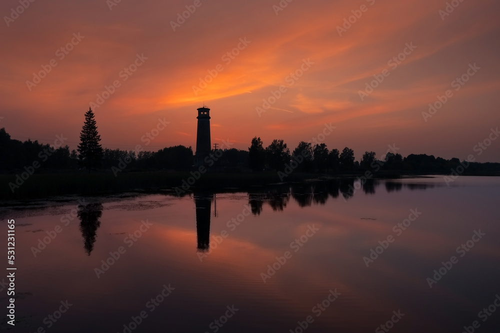 Sunset with silhouette of lighthouse and trees against colorful sky reflected in water Dubna Russia