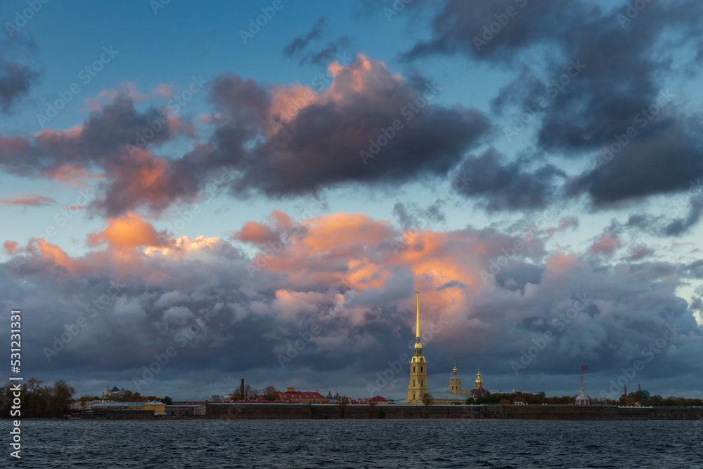 Fortress and high bell tower behind a river against cloudy colorful sunset sky, St.Petersburg Russia