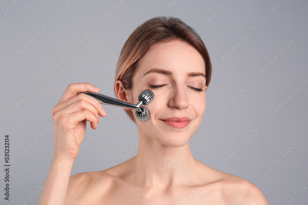 Young woman using metal face roller on light grey background Young woman using metal face roller on light grey background