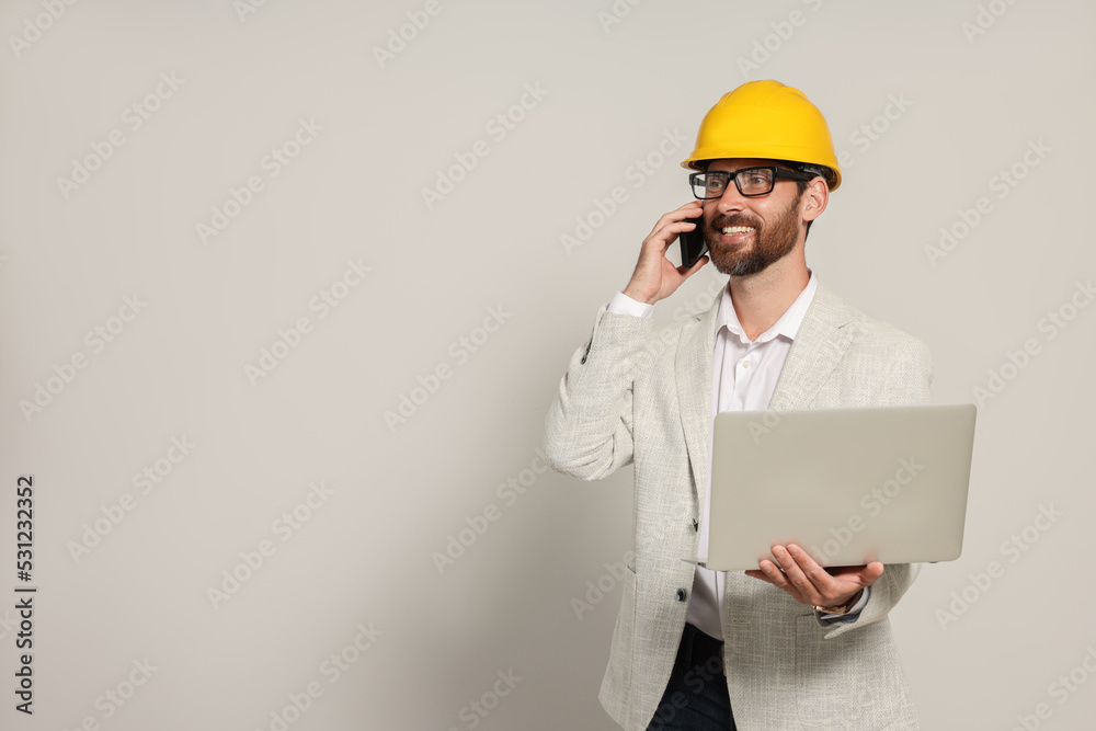 Professional engineer in hard hat with laptop talking on phone against white background, space for text Professional engineer in hard hat with laptop talking on phone against white background, space for text