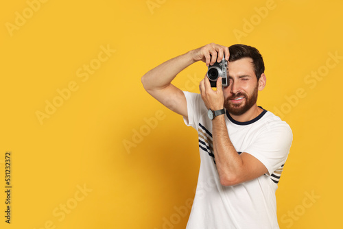 Man with camera taking photo on yellow background, space for text. Interesting hobby
