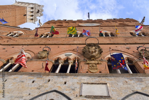 Fassade des Palazzo Pubblico mit Contradeflaggen und spitzen Dreibogenfenstern	 photo