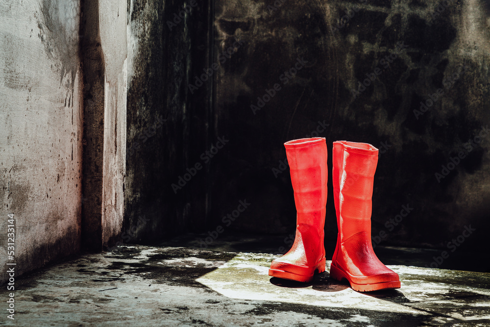 Pair of Red rubber rain boots with old bare cement wall background. Space for text, Selective focus.