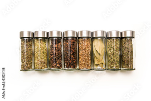 The different types of spices and herbs stored inside the small closable glass bottle isolated on a white background. 