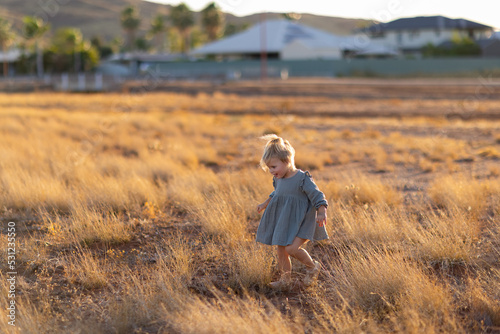 child running through dry grass with houses of town blurred in background
