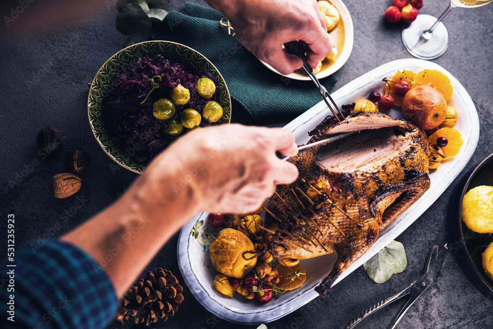 Obraz premium Christmas roast duck served on a festive table.man cuts the duck breast