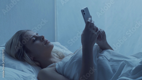 Obraz na plátně Young woman lying in the bed with a smartphone at night