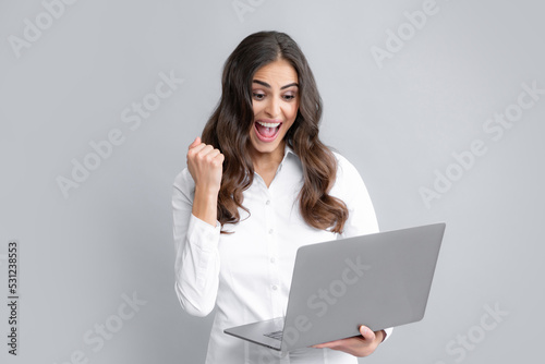 Portrait of a cheerful young casual girl standing isolated over gray background, using laptop computer. Business woman at work.