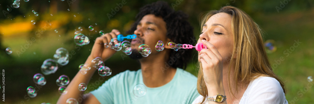 Mixed race couple blowing soap bubbles while sitting in the summer nature Mixed race couple blowing soap bubbles while sitting in the summer nature