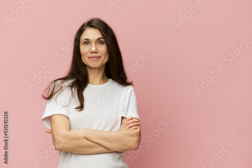 horizontal portrait of a cute, attractive woman on a pink background in a clean white t-shirt smiling pleasantly at the camera and folding her arms on her chest