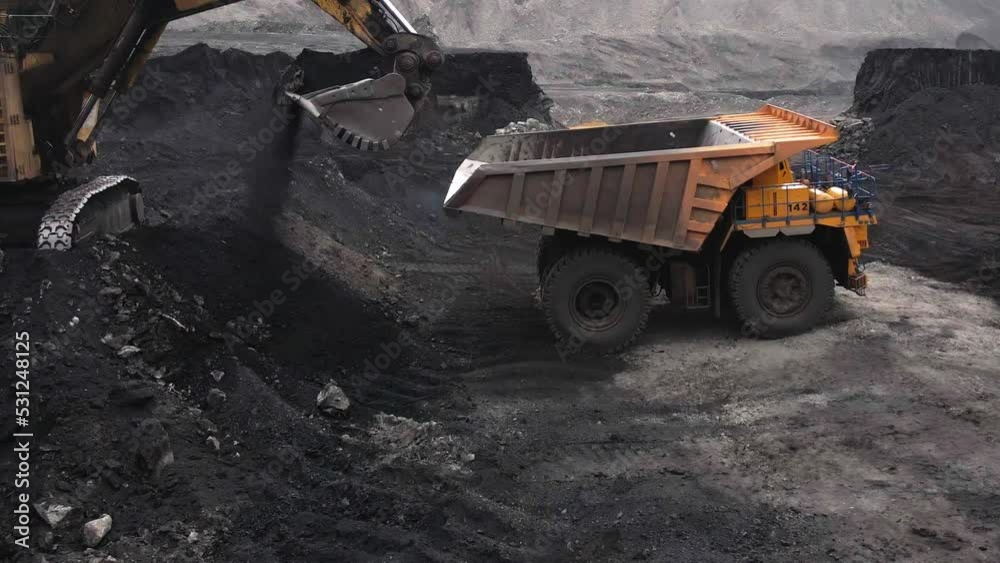 an old heavy excavator coaling onto the mining yellow dump truck . cinematic flight parallel the truck in a coal pit