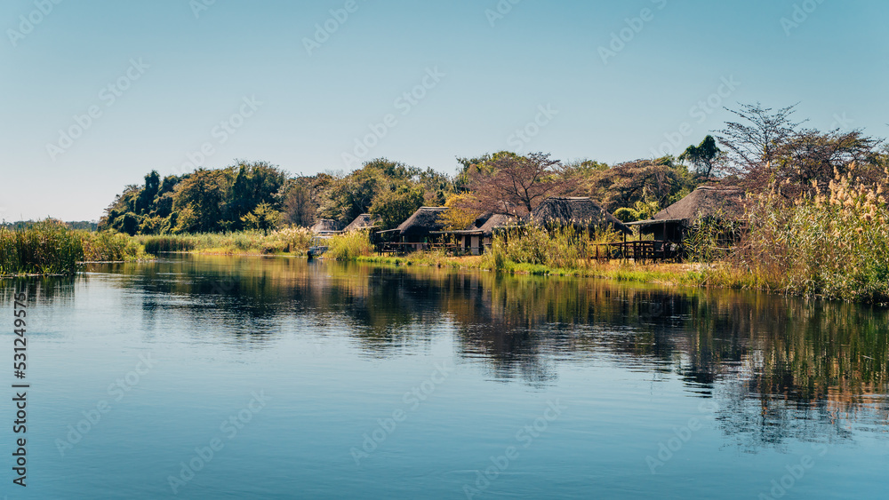 Idyllischer Blick auf eine Lodge am Ufer des Kwando River kurz nach Sonnenaufgang, Caprivi, Namibia