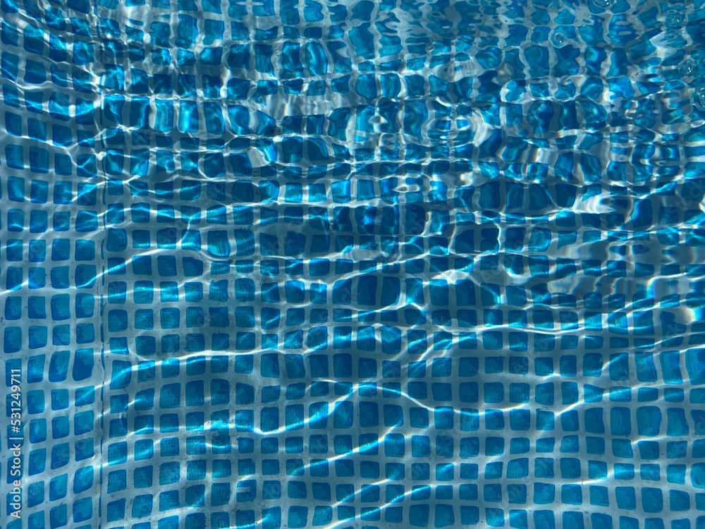 the blue checkered bottom of a pool through the water surface