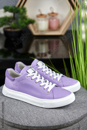 Stylish purple female shoes on gray pouf background in shop  copy space. New sneakers  close up. Beauty and fashion concept.