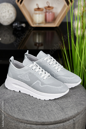 Stylish gray female shoes on gray pouf background in shop, copy space. New sneakers, close up. Beauty and fashion concept.
