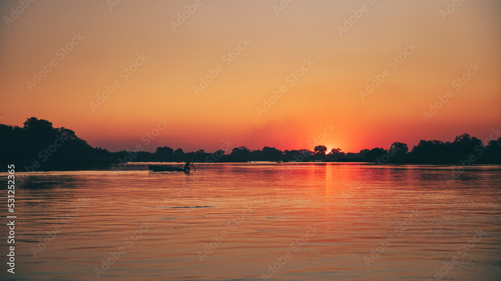 Idyllische Sonnenuntergangsszene am Okavango mit Boot-Silhouette (Namibia)