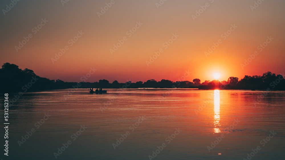 Idyllische Sonnenuntergangsszene am Okavango mit Boot-Silhouette (Namibia)