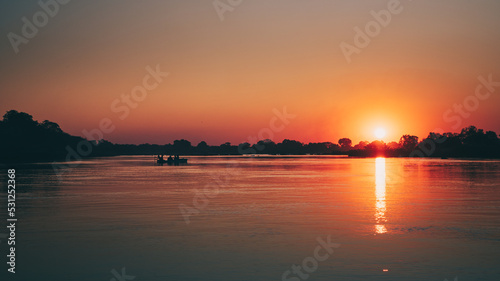 Idyllische Sonnenuntergangsszene am Okavango mit Boot-Silhouette (Namibia)