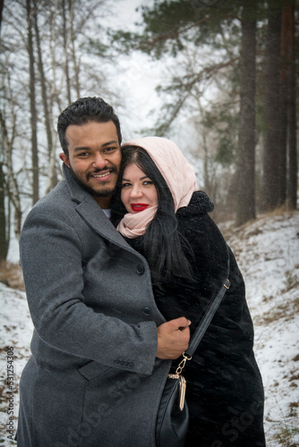 In winter, on a frosty day in the forest, a couple in love hugs.