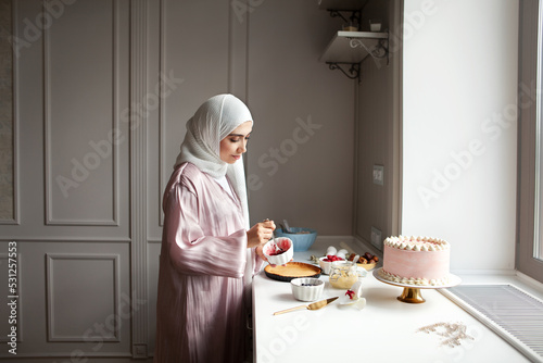 Muslim woman cooks dessert cake at home kitchen, arabian young model in hijab and abaya photo