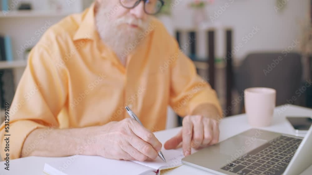 Closeup of senior man studying online while drinking tea at home, freelancer