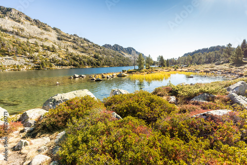 Lac de montagne aux eaux cristallines en automne avec buisson de raisin d'ours bruni au premier plan. Vallon d'Estibère, Réserve naturelle nationale du Néouvielle, Pyrénées photo