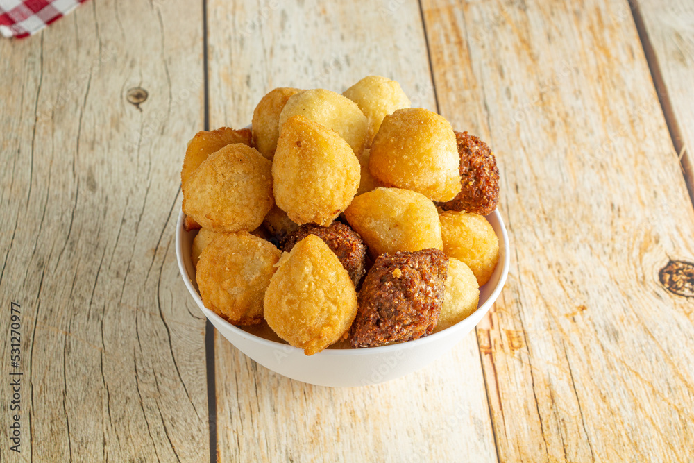 brazilian salgadinhos de festa, traditional party snack mix with coxinha, kibe, and other fried snacks over wooden table in a white container