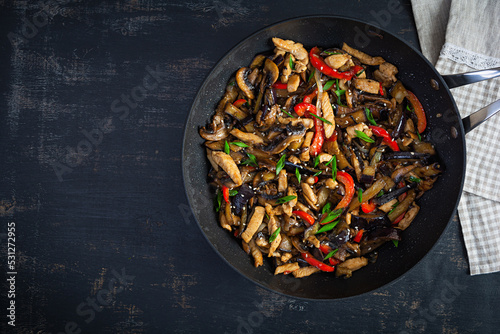 Stir fry with chicken, eggplant and pepper in wok pan on dark background