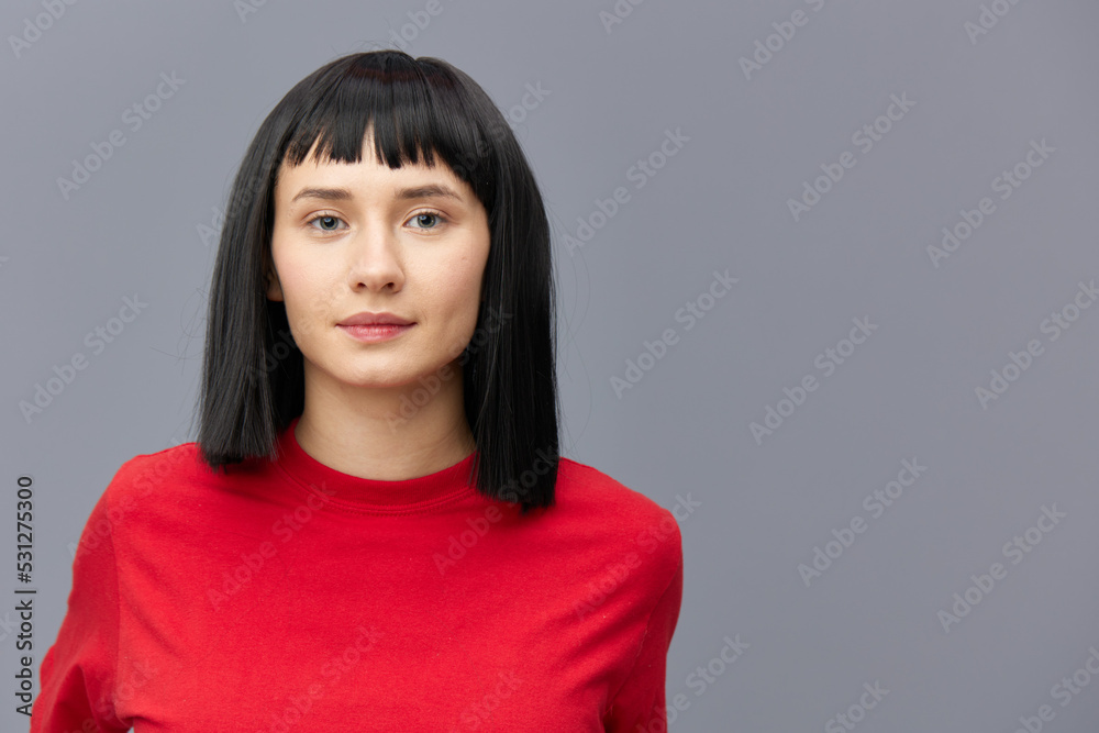 horizontal photo of a beautiful woman with short black hair looking pleasantly into the camera standing on a gray background in a red T-shirt horizontal photo of a beautiful woman with short black hair looking pleasantly into the camera standing on a gray background in a red T-shirt