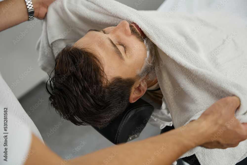 Caring barber removing foam from guest face with towel Caring barber removing foam from guest face with towel