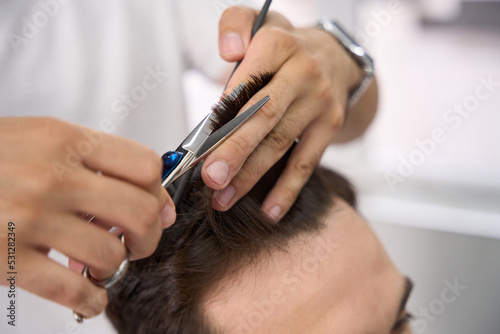 Skillful barber carefully cutting hair of his salon visitor