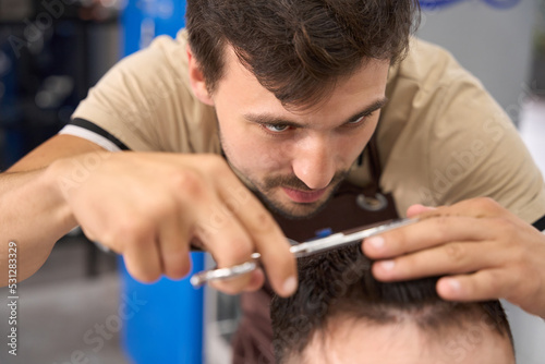 Focused young barbershop worker cutting hair of man