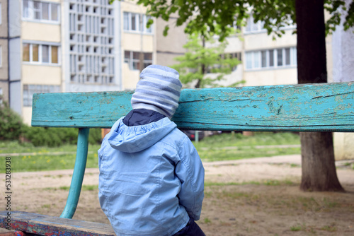 A sad boy is sitting on a bench with his back to the camera. The concept of anger, resentment and bullying on the street and at school © Ольга Мылица