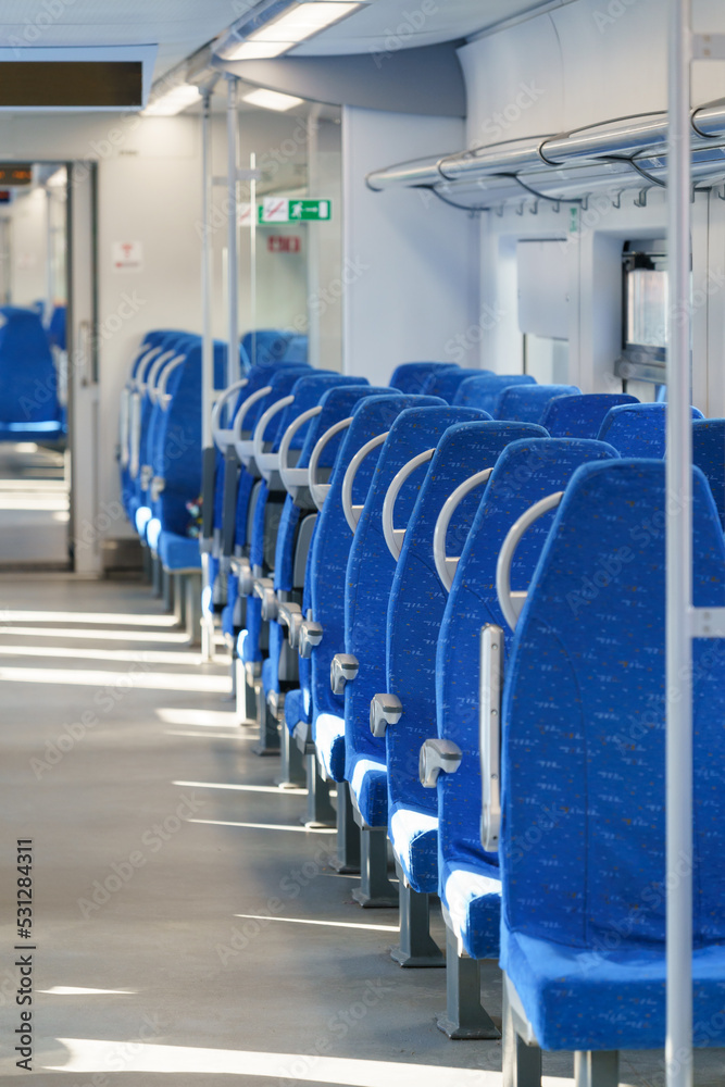 Fototapeta premium Interior of modern passenger high-speed express train, row of empty blue fabric soft seats selective soft focus. Inside the train carriage with comfortable and colorful chairs. Public transportation