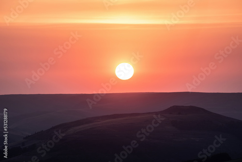 Beautiful late Summer sunset landscape image of setting sun kissing the horizon in the Peak District  viewed from Higger Tor