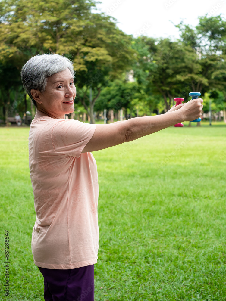 Portrait of mature asian woman 60s wearing sports clothing doing arm work out and lifting dumbbell exercise with relaxation for healthy in park outdoor. Portrait of mature asian woman 60s wearing sports clothing doing arm work out and lifting dumbbell exercise with relaxation for healthy in park outdoor.