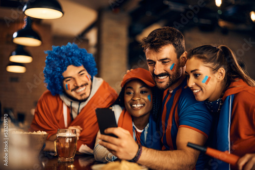 Obraz na płótnie Group of happy sports fans following match results on mobile phone in bar