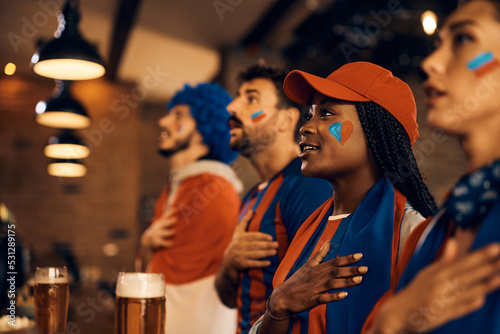 Group of fans with hand on heart singing national anthem while watching world cup in pub. photo
