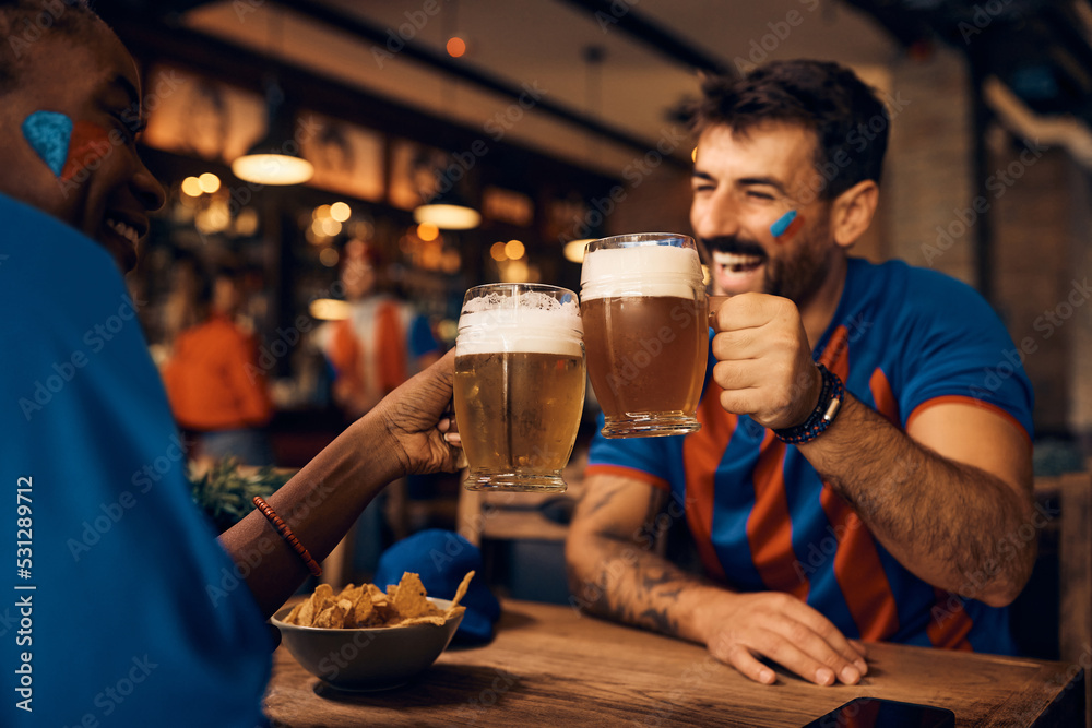 Close up of couple of soccer fans toasting with beer in pub.