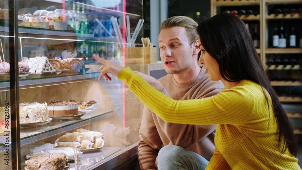 In the modern bakery cafe couple very beautiful looking choose the favourite desserts together from the showcase fridge