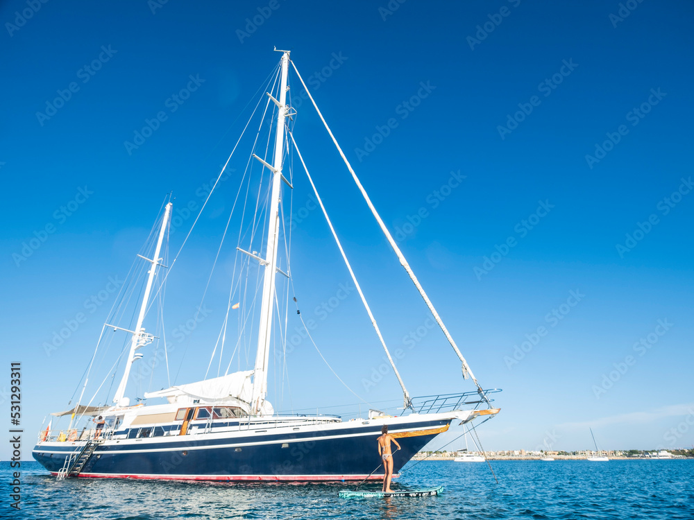 middle-aged woman practicing paddle surf next to a sailboat, Ses Covetes beach, Majorca, Balearic Islands, Spain middle-aged woman practicing paddle surf next to a sailboat, Ses Covetes beach, Majorca, Balearic Islands, Spain
