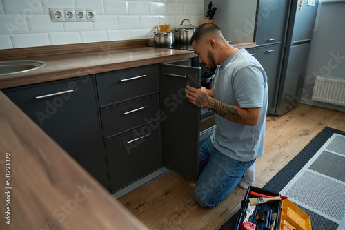 Canvas Print Man crouched at door of kitchen cabinet for minor repairs