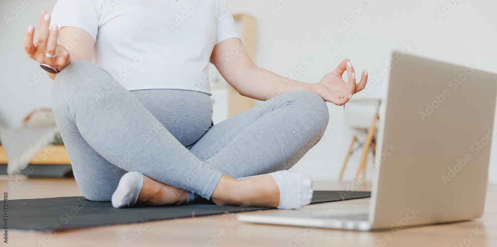 Young pregnant woman practicing online yoga at home with laptop, banner lifestyle pregnancy concept