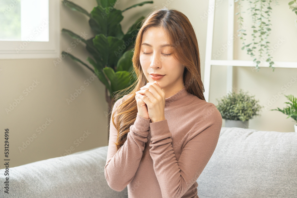Hopeful make wish, calm asian young woman belief, hand in prayer, sitting meditating on sofa at home, Christian girl praying to God for ask, request with closed eyes dreaming for help, thank you God. Hopeful make wish, calm asian young woman belief, hand in prayer, sitting meditating on sofa at home, Christian girl praying to God for ask, request with closed eyes dreaming for help, thank you God.