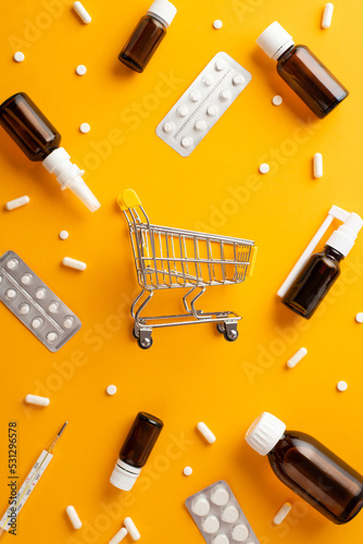 Healthcare concept. Top view vertical photo of pushcart remedy spray and syrup transparent brown bottles pills capsules and thermometer on isolated orange background