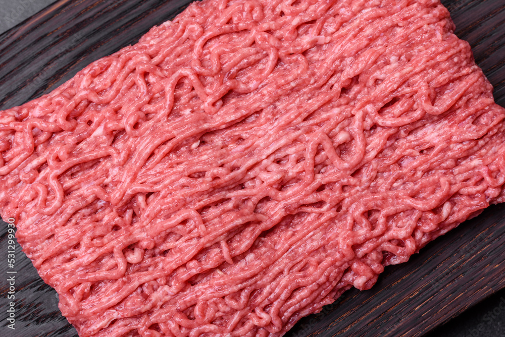 Fototapeta premium Fresh minced beef on cutting board on dark background with ingredients for cooking
