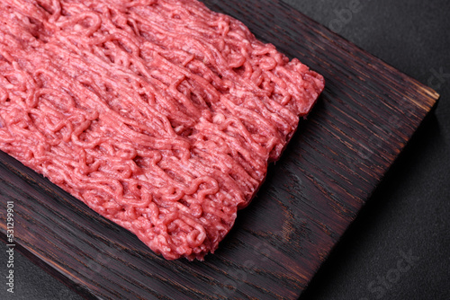 Fresh minced beef on cutting board on dark background with ingredients for cooking