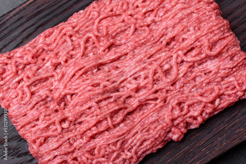 Fresh minced beef on cutting board on dark background with ingredients for cooking