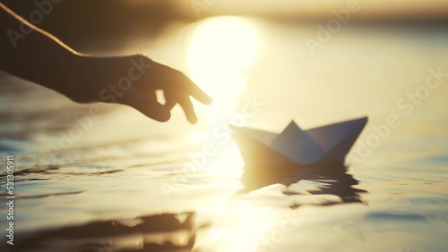 the child lowers the paper boat into the water. happy family fantasy child dream concept. a child plays with a paper boat ship. child's hand launches a boat in the park in the pond lifestyle