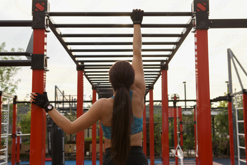 Rear view shot of a sportswoman climbing horizontal ladder, exercising outdoors